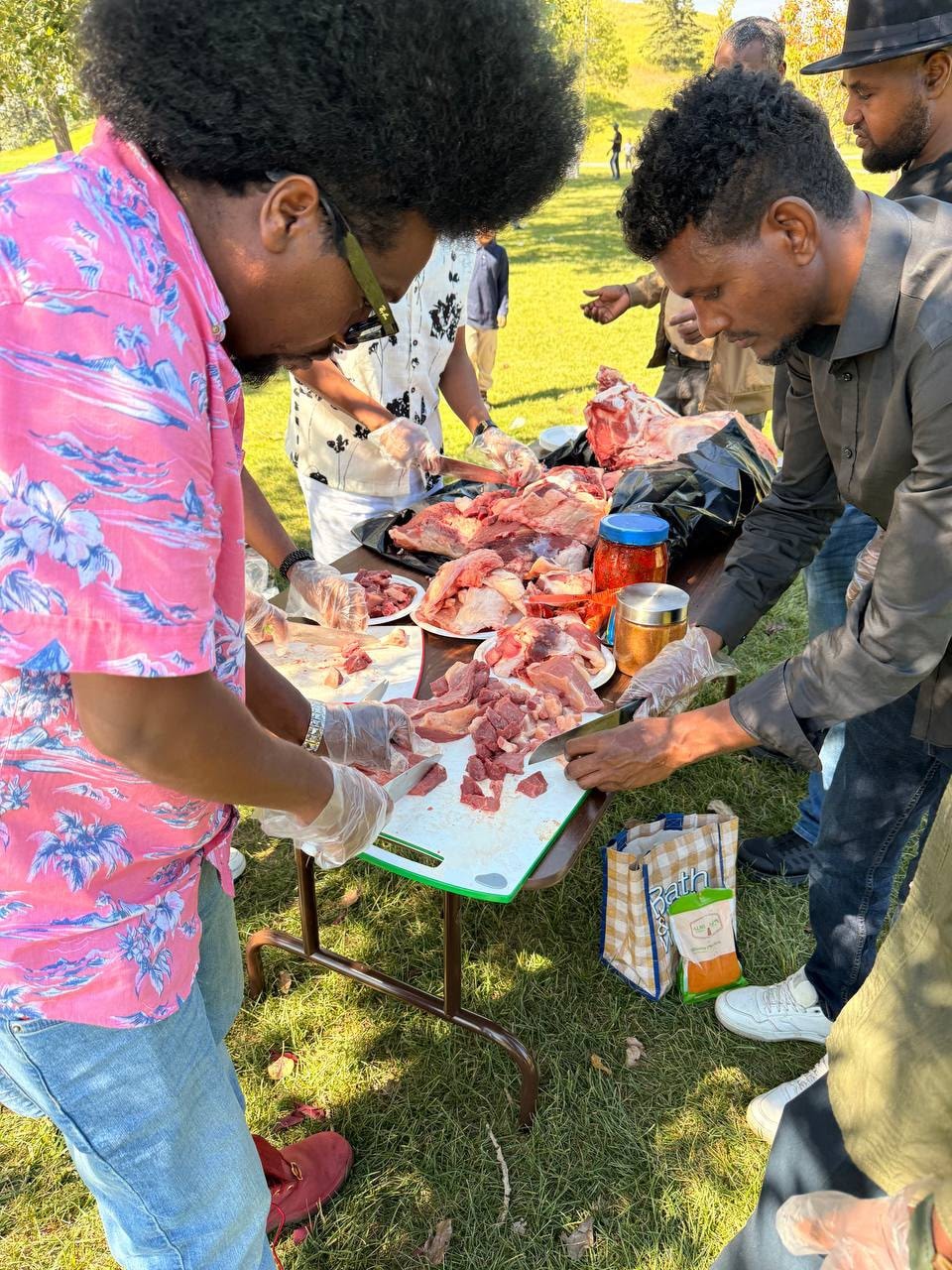 People preparing meat at an outdoor picnic table
