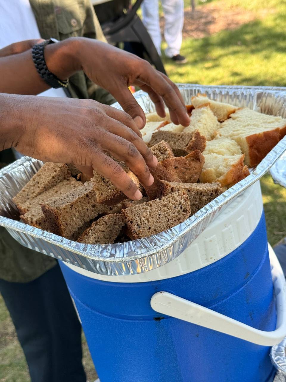 Hands reaching for bread slices at an outdoor picnic